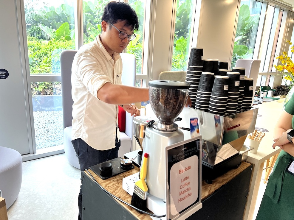 Barista grinding coffee beside an espresso machine and stacked cups