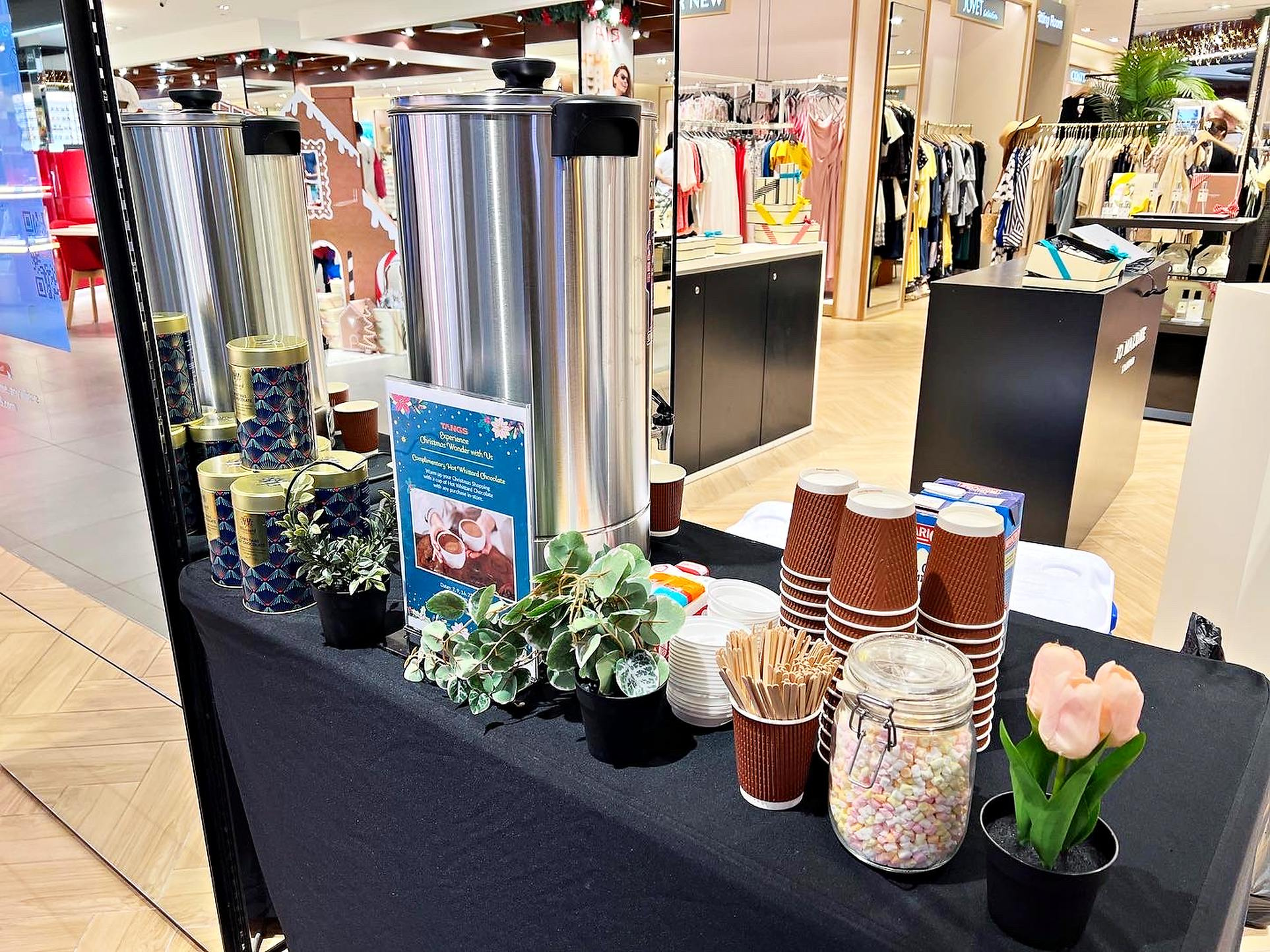 Hot chocolate station with cups and toppings beside metal urns