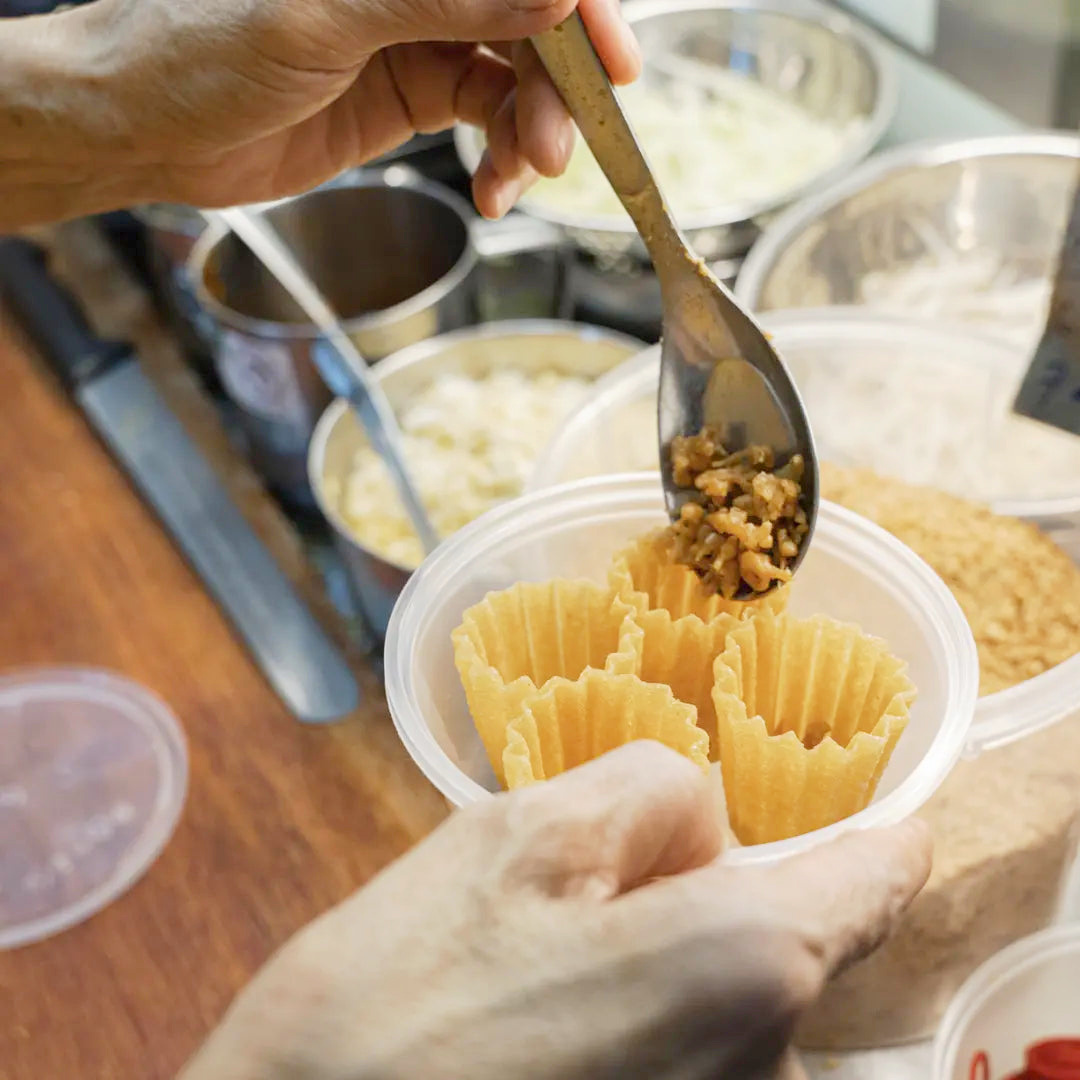 Gloved operator filling crispy kueh pie tee cups